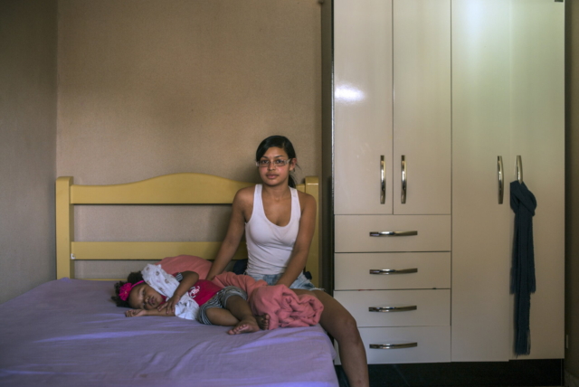 Dayane Lopes do Nascimento, 17, com a filha Maria Eduarda, 2. Dayane trabalha como caixa em um supermercado e, à noite, cursa o ensino médio. Ela e o namorado, de 25 anos, moram no bairro de São Miguel Paulista, em São Paulo, 2014, da série Offside Brazil. 30 x 42 cm. Foto de André Vieira. Coleção de Arte Contemporânea / Acervo IMS 