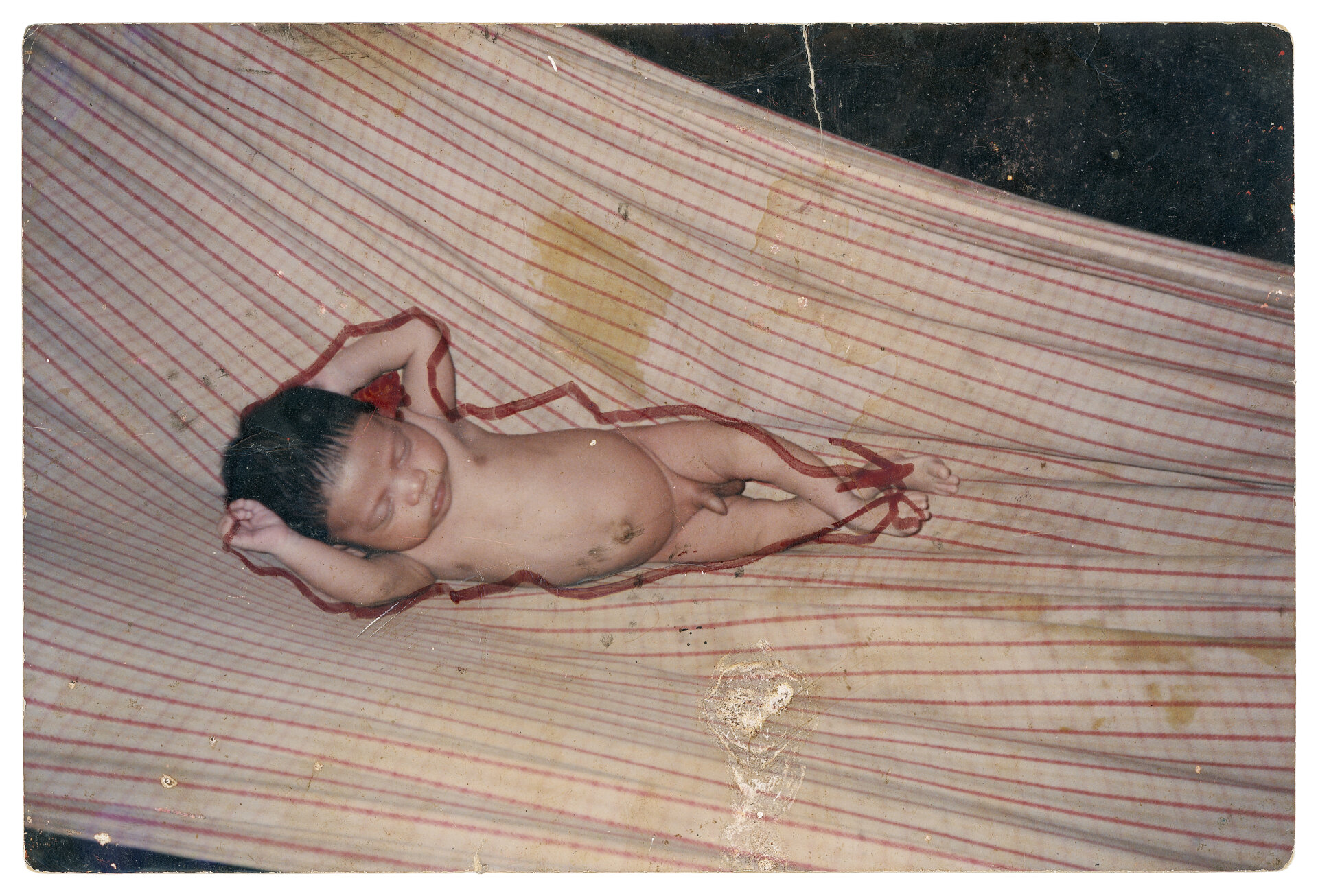 Manass&eacute;s Suru&iacute;, Aldeia Lapetanha, c. 1993 Muitas vezes, quando minha m&atilde;e n&atilde;o estava por perto, eu, Manass&eacute;s, e meus irm&atilde;os e primos nos reun&iacute;amos para olhar as fotos da fam&iacute;lia. Naquela &eacute;poca, as fotografias n&atilde;o tinham a mesma import&acirc;ncia que damos hoje, ent&atilde;o costum&aacute;vamos rabisc&aacute;-las com canetinhas. Faz&iacute;amos contornos das pessoas nas fotos, desenh&aacute;vamos barbas e bigodes nos rostos. Embora essas lembran&ccedil;as tragam um certo carinho, esta foto que o Almir tirou me remete a um tempo em que nossa fam&iacute;lia n&atilde;o tinha condi&ccedil;&otilde;es financeiras para comprar uma rede de dormir, nem mesmo roupas para os beb&ecirc;s. Nossas necessidades mudaram ap&oacute;s o contato com os brancos e, como n&atilde;o era da nossa cultura, levamos muitos anos para tentar nos adaptar a elas. Com isso, recordamos essa fase dif&iacute;cil de nossas vidas. Hoje, j&aacute; adultos, trabalhamos com a produ&ccedil;&atilde;o de caf&eacute;, banana, castanha e outros produtos, buscando gerar renda e proporcionar uma melhor qualidade de vida para nossa fam&iacute;lia. Foto de Almir Suru&iacute;. (Legenda por Coletivo Lakapoy).  Fotografias em pigmento mineral sobre papel de algod&atilde;o impressas em 2025. 92 x 63,2 cm. Cole&ccedil;&atilde;o de Arte Contempor&acirc;nea / Acervo IMS 