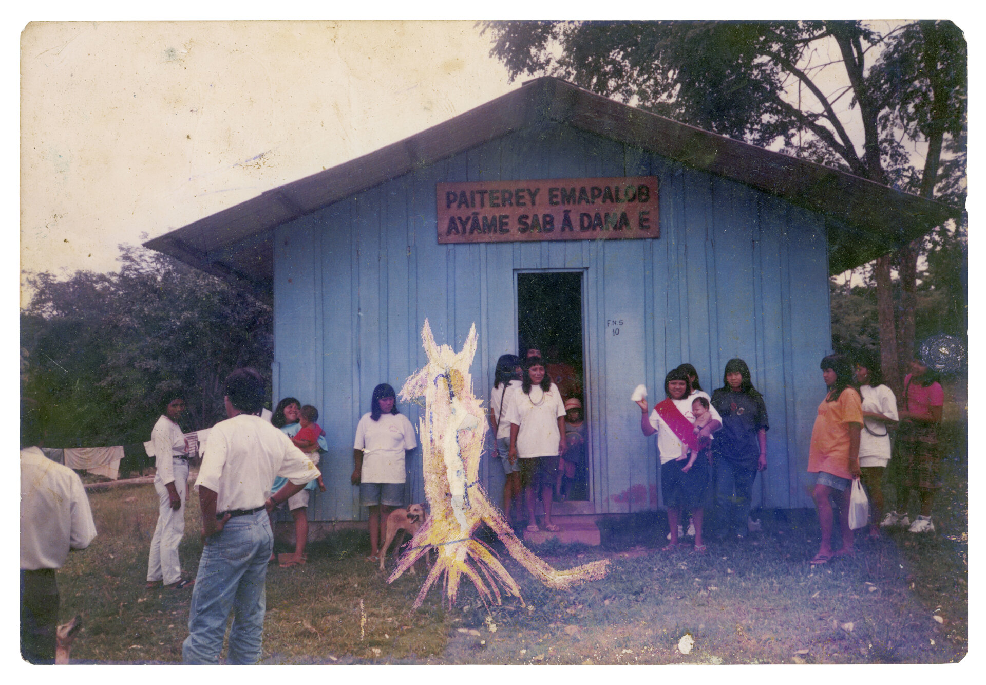  Rosely (n&atilde;o ind&iacute;gena), Lourdes com filho, Kabena Cinta Larga, Raimunda Cinta Larga (na porta), Elza Pamoga Suru&iacute; (com beb&ecirc; na tipoia), Gisele Suru&iacute; e outros Paiter Suru&iacute;, Aldeia Lib&oacute;, c. 1982 Esta &eacute; a igreja batista da aldeia Lob&oacute;, na Linha 11. A placa diz &ldquo;Casa de adora&ccedil;&atilde;o do povo de Deus&rdquo; em tupi-mond&eacute;. Uma crian&ccedil;a rabiscou a forma de um dem&ocirc;nio na imagem para esconder um ind&iacute;gena que havia cometido homic&iacute;dio dentro da comunidade. Ele e a fam&iacute;lia foram expulsos do territ&oacute;rio como forma de puni&ccedil;&atilde;o por n&atilde;o terem seguido as regras da nossa cultura. Autoria desconhecida. (Legenda por Coletivo Lakapoy).  Fotografias em pigmento mineral sobre papel de algod&atilde;o impressas em 2025. 77 x 54,2 cm. Cole&ccedil;&atilde;o de Arte Contempor&acirc;nea / Acervo IMS 
