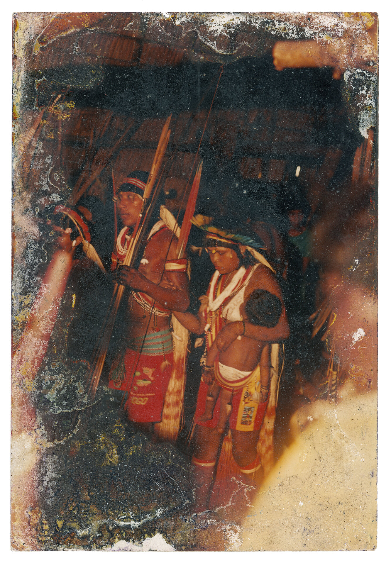 Napo Suru&iacute; e Elza Pamoga Suru&iacute;, Aldeia Gabgir, anos 1990 O casal Napo e Pamoga durante o Mapimai &ndash; ritual em que comemoramos a cria&ccedil;&atilde;o do mundo. No passado, &eacute;ramos divididos em v&aacute;rios cl&atilde;s, mas as guerras e, principalmente, o contato diminu&iacute;ram drasticamente nossa popula&ccedil;&atilde;o. Hoje s&oacute; restaram Gameb, Makor e Gabgir, todos de linhagem pr&oacute;xima, e Kaban, que surgiu de uma mistura com o povo Cinta Larga, etnia tamb&eacute;m falante do tupi-mond&eacute;. Nessas cerim&ocirc;nias, participam apenas dois grupos, que travam uma disputa com o uso da chicha, bebida fermentada que pode ser de mandioca, car&aacute;, milho ou batata-doce. O cl&atilde; anfitri&atilde;o prepara centenas de litros, e os convidados t&ecirc;m que beber tudo at&eacute; o final, caso contr&aacute;rio s&atilde;o tidos como derrotados. Artesanatos devem ser oferecidos em troca da bebida, e a festa tamb&eacute;m envolve pintura, m&uacute;sica e dan&ccedil;a. Antes do contato, que aconteceu em 1969, o ritual era comum e durava v&aacute;rias semanas, mas hoje raramente acontece. Autoria desconhecida. (Legenda por Coletivo Lakapoy).  Fotografias em pigmento mineral sobre papel de algod&atilde;o impressas em 2025. 52 x 74 cm. Cole&ccedil;&atilde;o de Arte Contempor&acirc;nea / Acervo IMS 