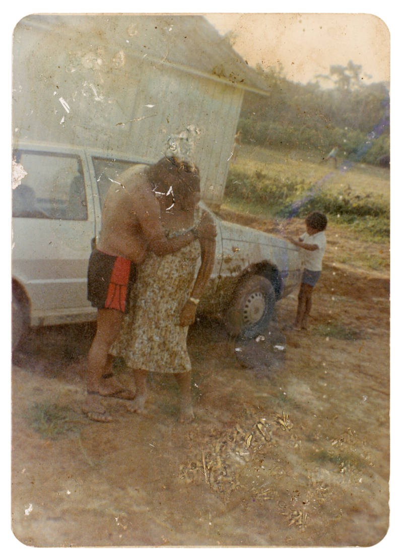 7 - Itabira Suru&iacute; e Sandra Suru&iacute; e crian&ccedil;a Paiter Suru&iacute; Aldeia Lapetanha, anos 1990 A conviv&ecirc;ncia com os brancos introduziu novos costumes e valores no territ&oacute;rio Paiter Suru&iacute;. Nesta foto, Itabira havia decidido expressar seu amor por Sandra com um beijo na boca da esposa. A demonstra&ccedil;&atilde;o, por&eacute;m, foi motivo de gargalhadas para os ind&iacute;genas presentes, j&aacute; que o ato do casal tocando os l&aacute;bios n&atilde;o existia na cultura Paiter, ou seja, n&atilde;o havia beijo na boca antes do contato com os n&atilde;o ind&iacute;genas. Autoria desconhecida. (Legenda por Coletivo Lakapoy).  Fotografias em pigmento mineral sobre papel de algod&atilde;o impressas em 2025. 52 x 71,5 cm. Cole&ccedil;&atilde;o de Arte Contempor&acirc;nea / Acervo IMS   