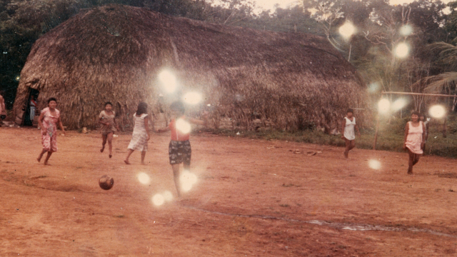 Jogo de futebol feminino, Aldeia Lapetanha, c. 1986
As partidas de futebol entre as aldeias Lapetanha e Joaquim marcaram época. As mulheres jogavam equipadas apenas com vestidos fornecidos pela Funai. Esses jogos, que também envolviam outros clãs, davam prêmios para os vencedores, que incluíam artesanatos, carne de caça e outros itens tradicionais, transformando-se em um importante momento de integração entre as comunidades. A rivalidade saudável e a troca de presentes criavam um clima de festa e união, fortalecendo os laços entre os diferentes grupos e núcleos familiares. Foto da missionaria Tine Wand Mer. (Legenda por Coletivo Lakapoy). 
Fotografias em pigmento mineral sobre papel de algodão impressas em 2025. 92 x 67,3 cm. Coleção de Arte Contemporânea / Acervo IMS
